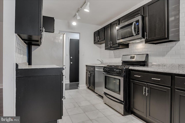 kitchen with light stone counters, light tile patterned floors, tasteful backsplash, appliances with stainless steel finishes, and dark cabinets