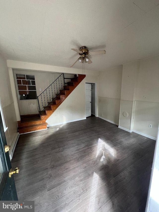 unfurnished living room with a baseboard heating unit, a ceiling fan, dark wood-style flooring, and stairs