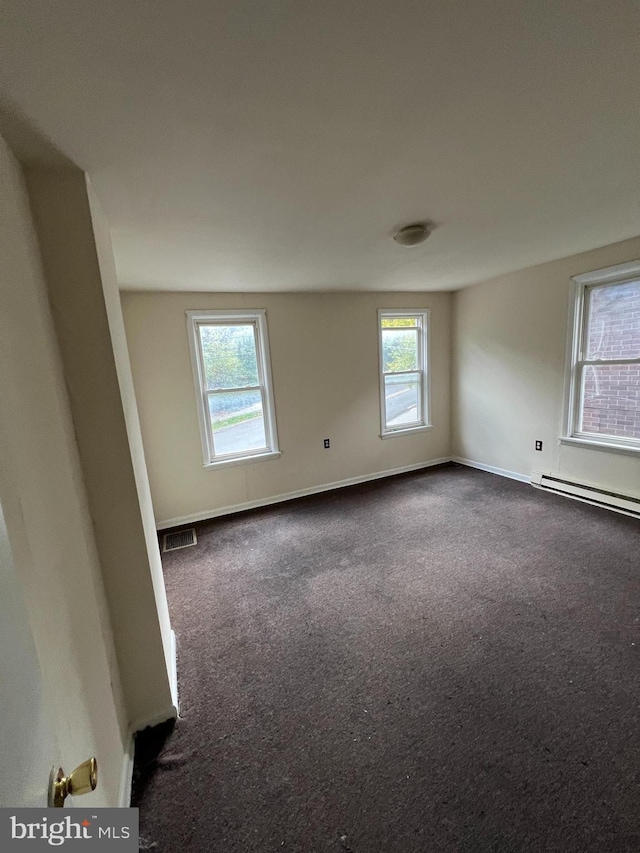 spare room featuring baseboards, visible vents, a baseboard heating unit, and dark colored carpet