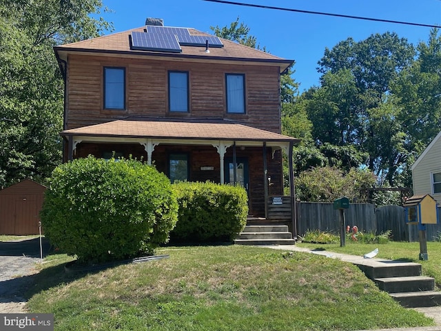 view of front of property featuring a front yard, solar panels, a shed, and a porch