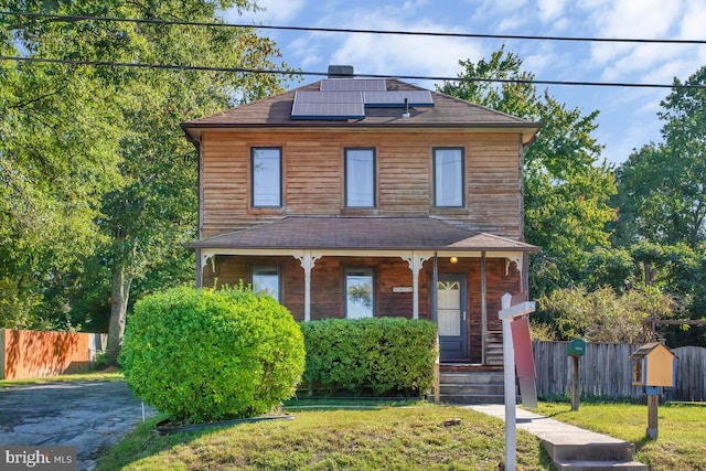 view of front facade featuring covered porch, a front lawn, and solar panels