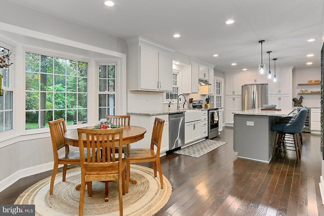 kitchen with light stone counters, stainless steel appliances, hanging light fixtures, and white cabinetry