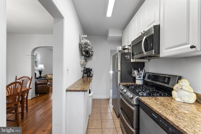 kitchen with appliances with stainless steel finishes, white cabinetry, light hardwood / wood-style flooring, and dark stone counters