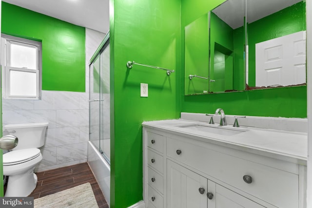 full bathroom with enclosed tub / shower combo, tile patterned floors, toilet, tile walls, and vanity