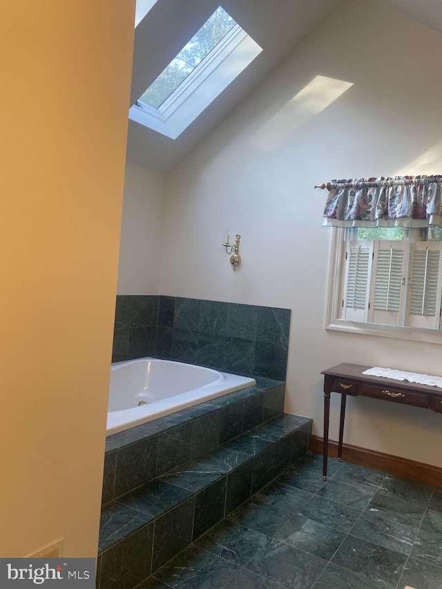 bathroom with lofted ceiling, tiled bath, and plenty of natural light