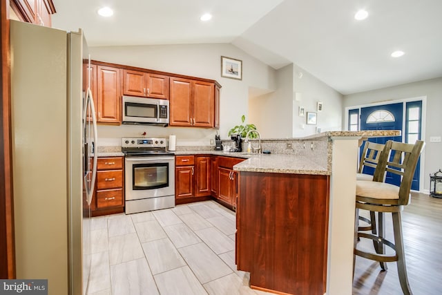 kitchen featuring vaulted ceiling, a breakfast bar area, appliances with stainless steel finishes, kitchen peninsula, and light stone counters