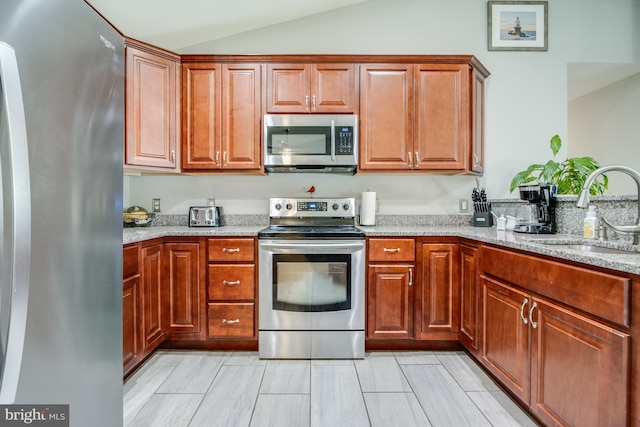 kitchen with appliances with stainless steel finishes, light stone counters, vaulted ceiling, and sink