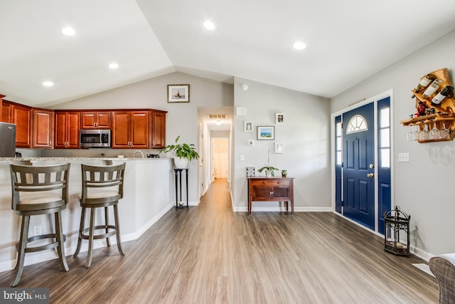 kitchen featuring vaulted ceiling, hardwood / wood-style flooring, stainless steel appliances, and a kitchen breakfast bar