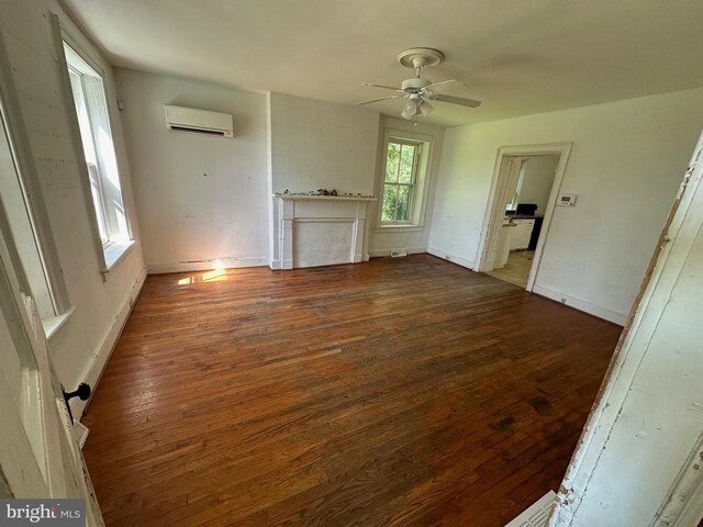 unfurnished living room with an AC wall unit, dark wood-style flooring, a ceiling fan, and baseboards