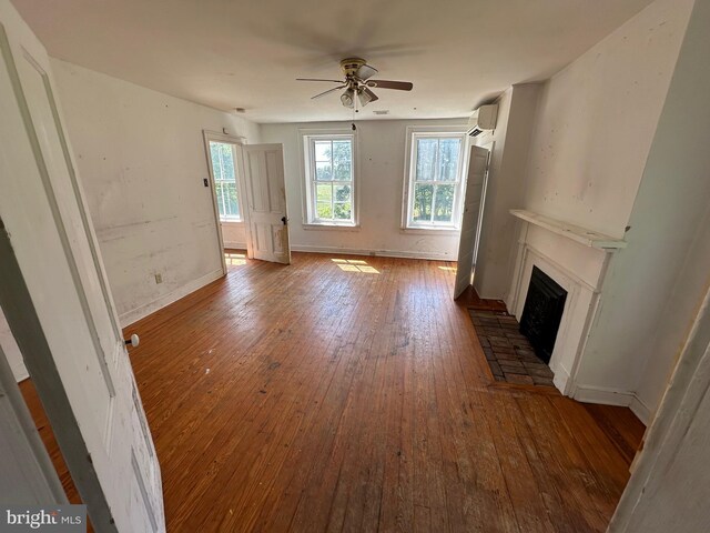 unfurnished living room featuring baseboards, a fireplace with raised hearth, ceiling fan, dark wood-style flooring, and a wall mounted air conditioner