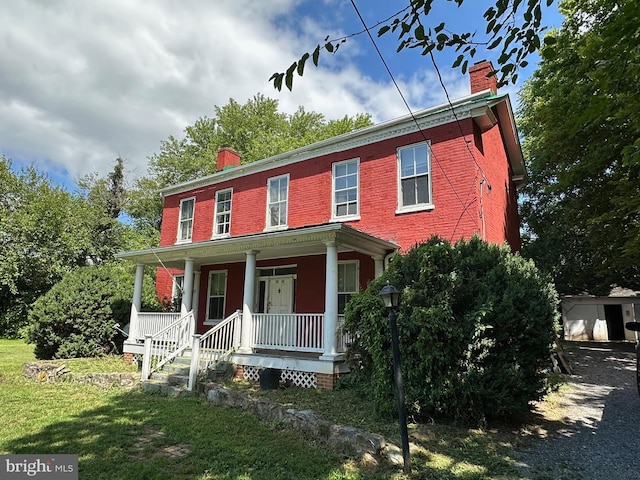 colonial-style house featuring a porch, brick siding, a chimney, and a front lawn