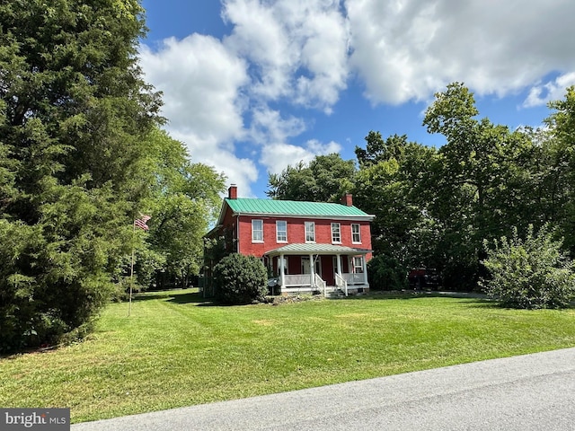 colonial-style house featuring a chimney, covered porch, a front yard, a standing seam roof, and metal roof