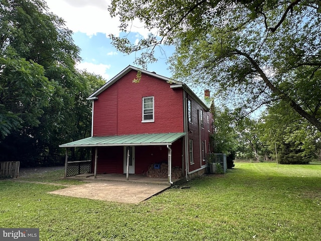 back of house featuring brick siding, a yard, a chimney, a patio area, and metal roof