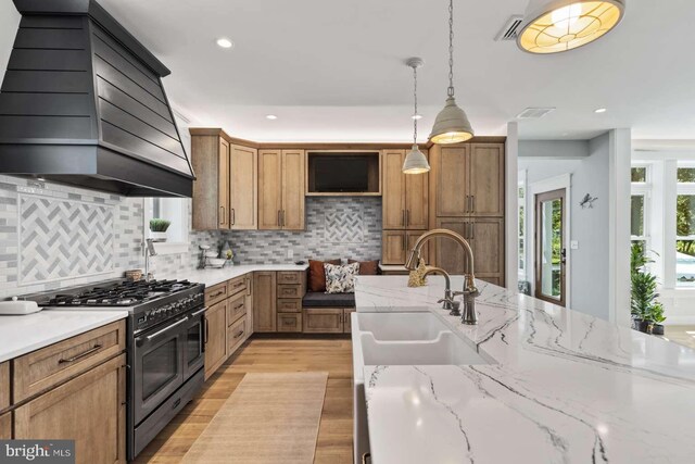 kitchen with premium range hood, light hardwood / wood-style floors, decorative backsplash, sink, and range with two ovens