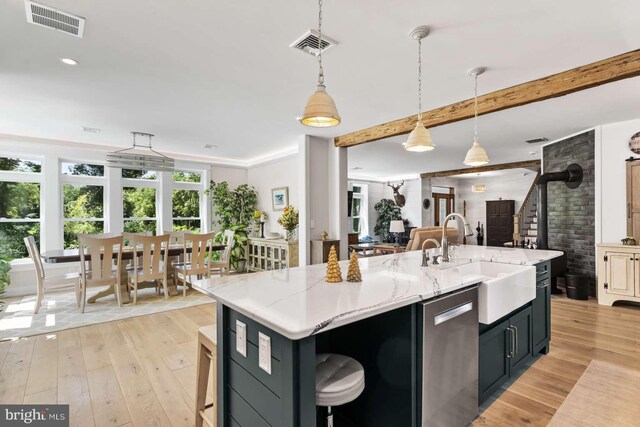 kitchen with light hardwood / wood-style floors, stainless steel dishwasher, a center island with sink, and decorative light fixtures