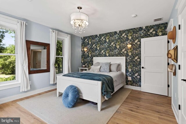 bedroom featuring multiple windows, light hardwood / wood-style floors, and a chandelier