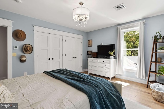 bedroom featuring light wood-type flooring, an inviting chandelier, and a closet