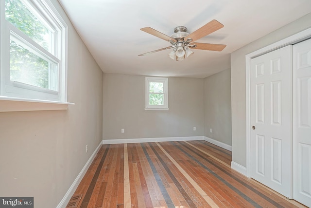 unfurnished bedroom with a closet, ceiling fan, hardwood / wood-style floors, and multiple windows