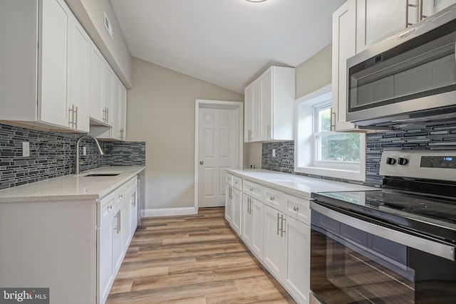 kitchen with light wood-type flooring, tasteful backsplash, white cabinets, lofted ceiling, and stainless steel appliances