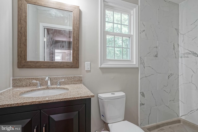 bathroom with a tile shower, vanity, and toilet