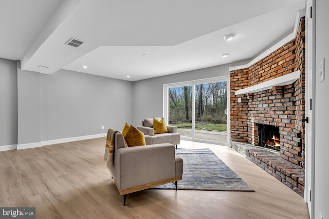 living room with a fireplace, light wood-type flooring, and brick wall