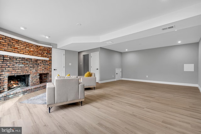 living room featuring light wood-type flooring, brick wall, and a brick fireplace