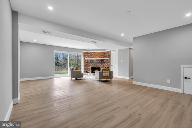 unfurnished living room with brick wall, light hardwood / wood-style flooring, and a brick fireplace