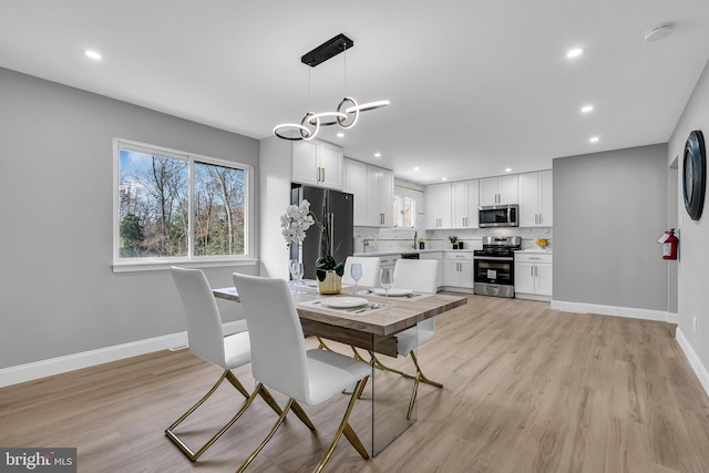 dining space featuring light wood-type flooring, sink, and an inviting chandelier