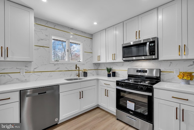 kitchen with backsplash, stainless steel appliances, light hardwood / wood-style flooring, white cabinetry, and sink