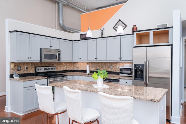 kitchen featuring tasteful backsplash, visible vents, a center island, appliances with stainless steel finishes, and a towering ceiling
