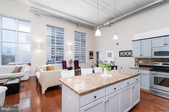 kitchen with light stone countertops, tasteful backsplash, a towering ceiling, electric stove, and dark wood-style floors