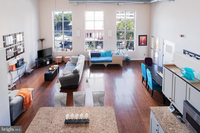 living area featuring dark wood-type flooring, a towering ceiling, and baseboards