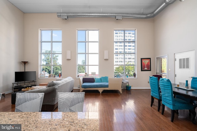 living room with dark wood-type flooring, plenty of natural light, a high ceiling, and baseboards