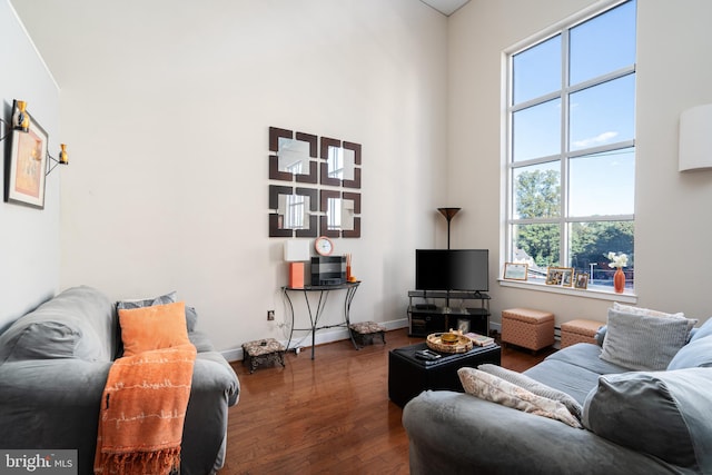 living room with dark wood-type flooring, a towering ceiling, and baseboards