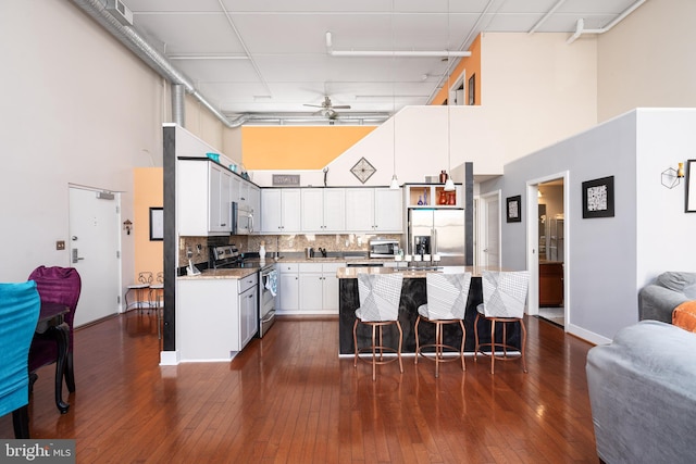 kitchen featuring tasteful backsplash, a towering ceiling, a kitchen island, appliances with stainless steel finishes, and white cabinetry