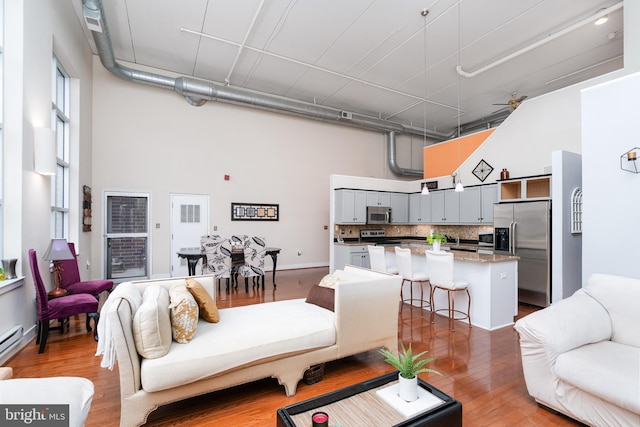 living area with a towering ceiling, baseboards, a ceiling fan, and wood finished floors