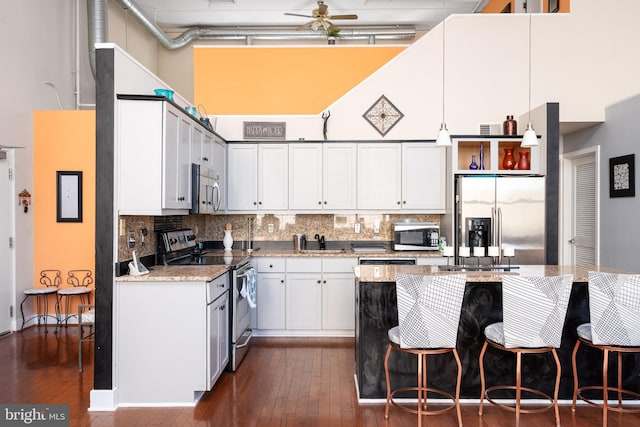 kitchen with stainless steel appliances, white cabinetry, a towering ceiling, light stone countertops, and tasteful backsplash