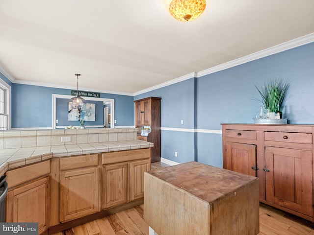 kitchen featuring light hardwood / wood-style flooring, ornamental molding, a center island, and tile countertops