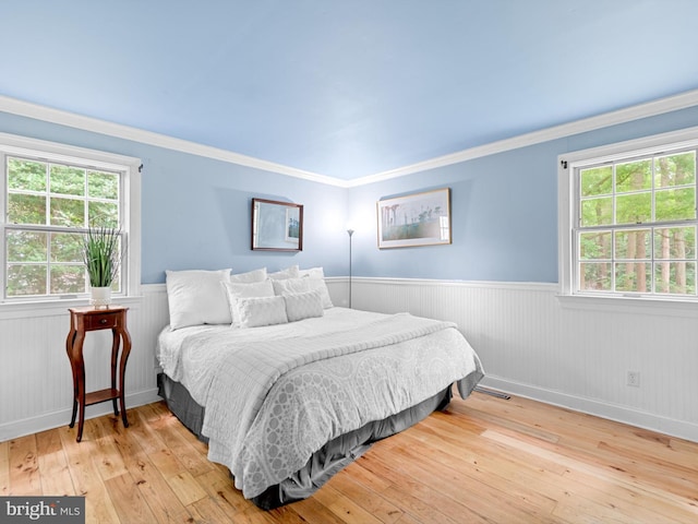 bedroom with light wood-type flooring, multiple windows, and crown molding