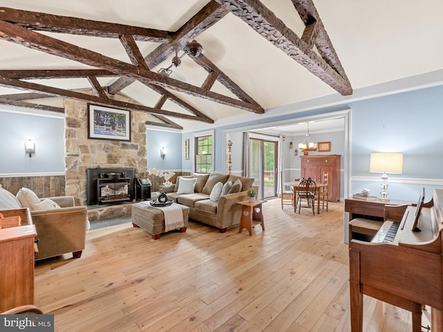 living room with a notable chandelier, a stone fireplace, light wood-type flooring, and vaulted ceiling with beams