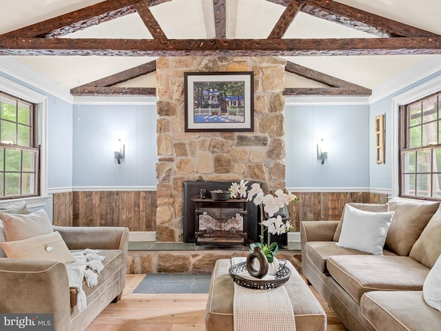 living room with a wealth of natural light, vaulted ceiling with beams, hardwood / wood-style floors, and a stone fireplace