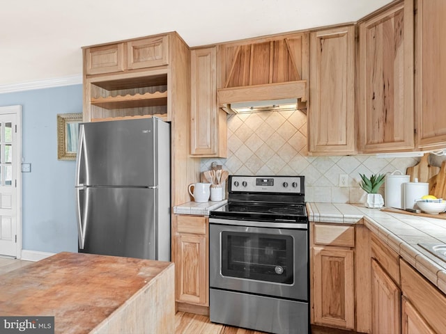 kitchen with backsplash, crown molding, tile countertops, appliances with stainless steel finishes, and light hardwood / wood-style floors