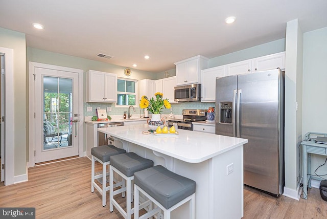 kitchen with a center island, stainless steel appliances, white cabinetry, and light hardwood / wood-style floors