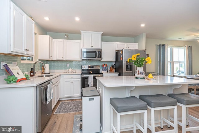 kitchen with light hardwood / wood-style flooring, stainless steel appliances, a kitchen island, sink, and white cabinets