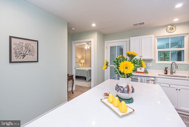 kitchen with backsplash, dishwasher, light hardwood / wood-style floors, white cabinetry, and sink