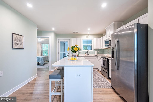 kitchen with a healthy amount of sunlight, a kitchen island, stainless steel appliances, and light hardwood / wood-style floors