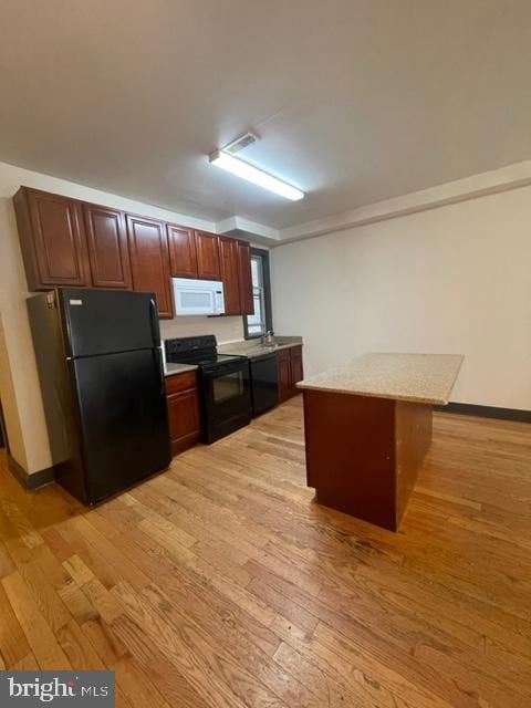 kitchen with black appliances, light hardwood / wood-style flooring, and light stone countertops