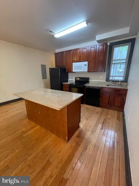 kitchen with a center island, light wood-type flooring, light stone counters, sink, and black appliances