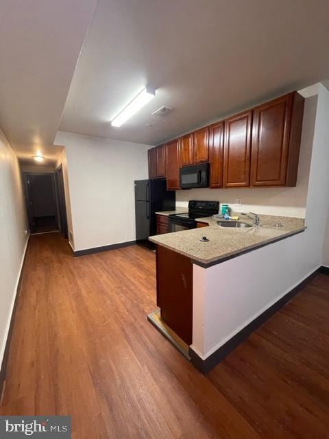 kitchen with light wood-type flooring, black appliances, kitchen peninsula, sink, and light stone countertops