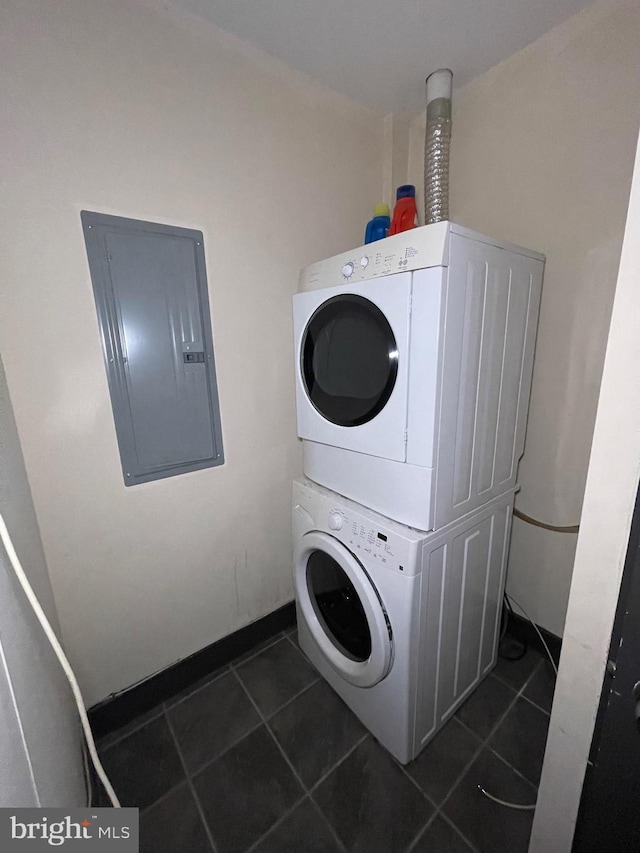 washroom featuring electric panel, stacked washer and clothes dryer, and dark tile patterned floors